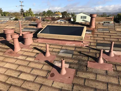Before stone coat: primed pink vents and flashings on a terracotta roof