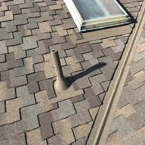 Stone coated pipe beside a skylight and valley on brown shingles