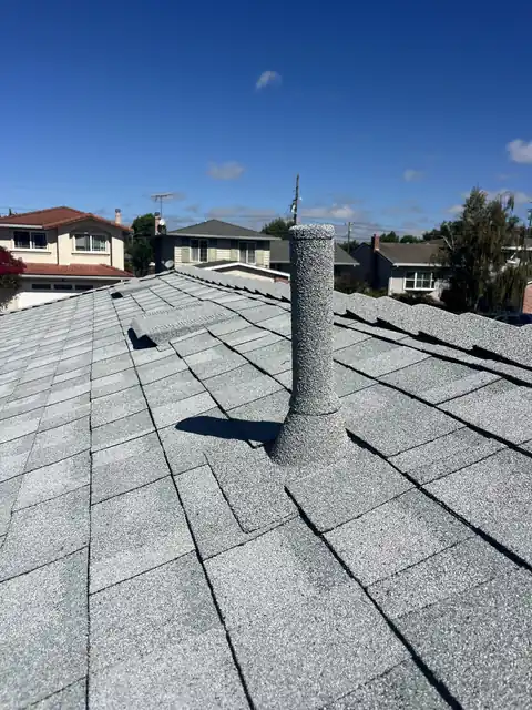 Grey stone coated pipe on a light grey roof, houses behind