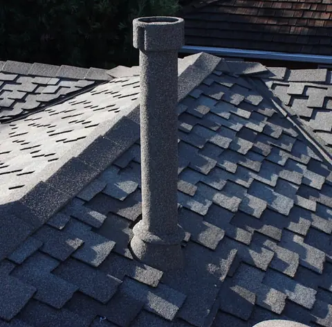 Tall dark stone coated pipe on dark architectural shingles