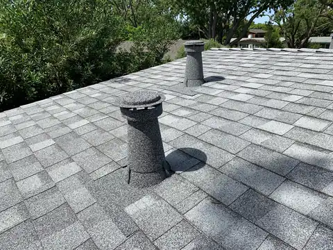 Grey stone coated vent with a cap on a platinum shingle roof