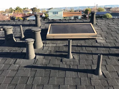A set of stone coated vents and a skylight on a dark roof with the bay beyond