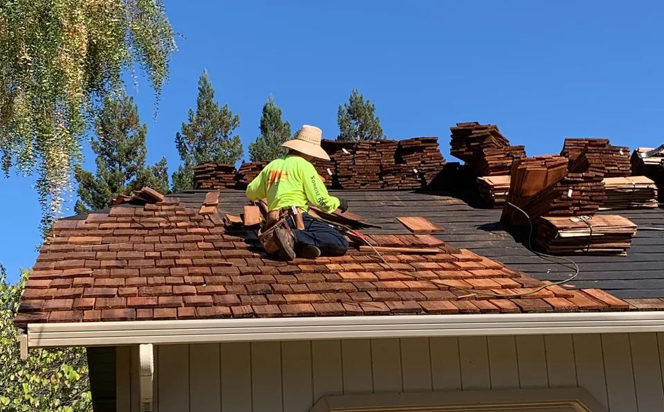 Roofer working on a roof over a garage with bundles stacked on the deck