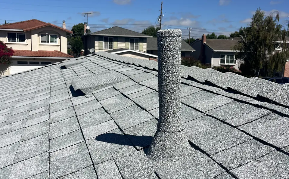 Grey stone coated pipe sleeve on a light grey shingle roof, houses behind