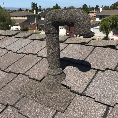 Grey stone coated elbow vent on a grey shingle roof, houses behind
